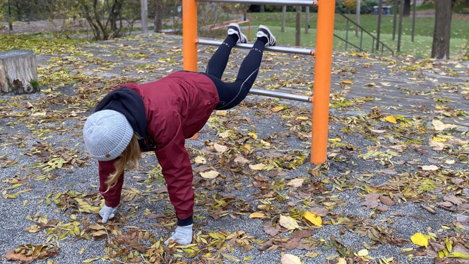 Ung kvinna tränar på ett modernt utegym i en lummig park.
