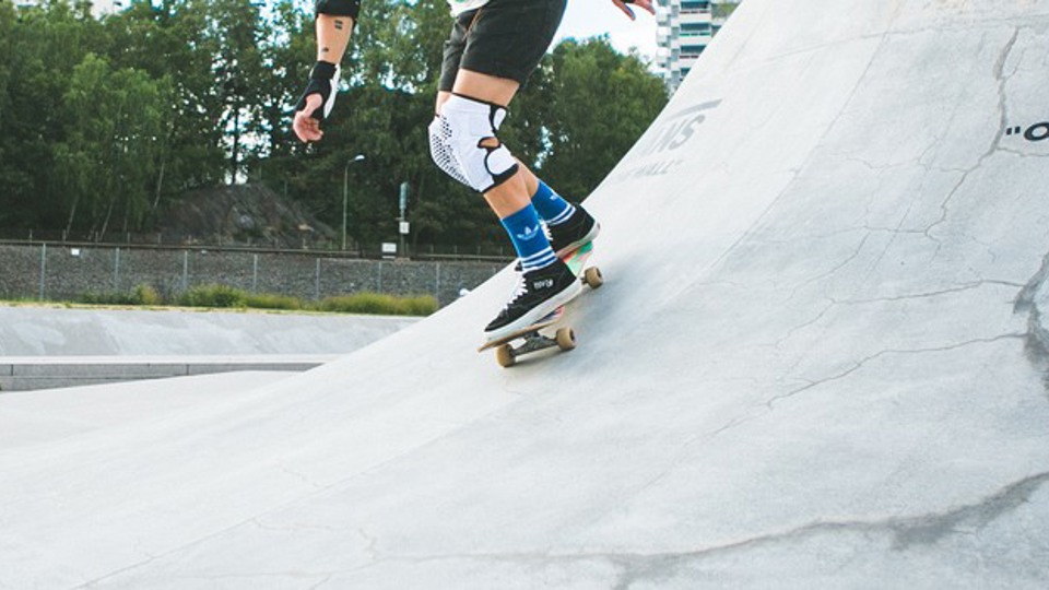 En person med knä- och handledsskydd åker skateboard i en skateramp.