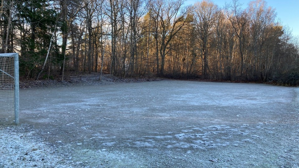 Frosttäckt grusplan med fotbollsmål och skog runtom.