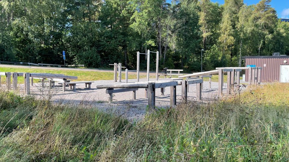 Gymredskap i trä som står på ett grusunderlag med träd intill.