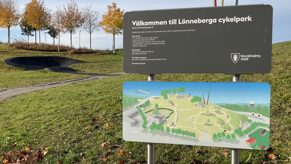 Skylt över Lönneberga cykelpark med grönyta och cykelbana i bakgrunen