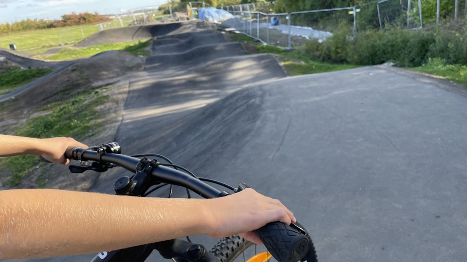 En person håller i ett cykelstyre. Framför personen slingrar sig en guppig asfalterad bana.