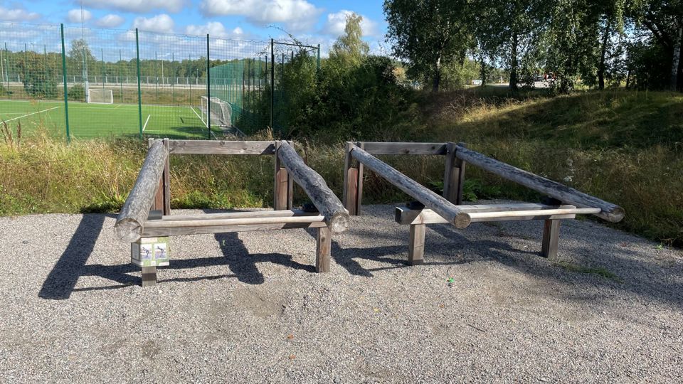 Gymredskap i trä som står på ett grusunderlag invid en fotbollsplan.