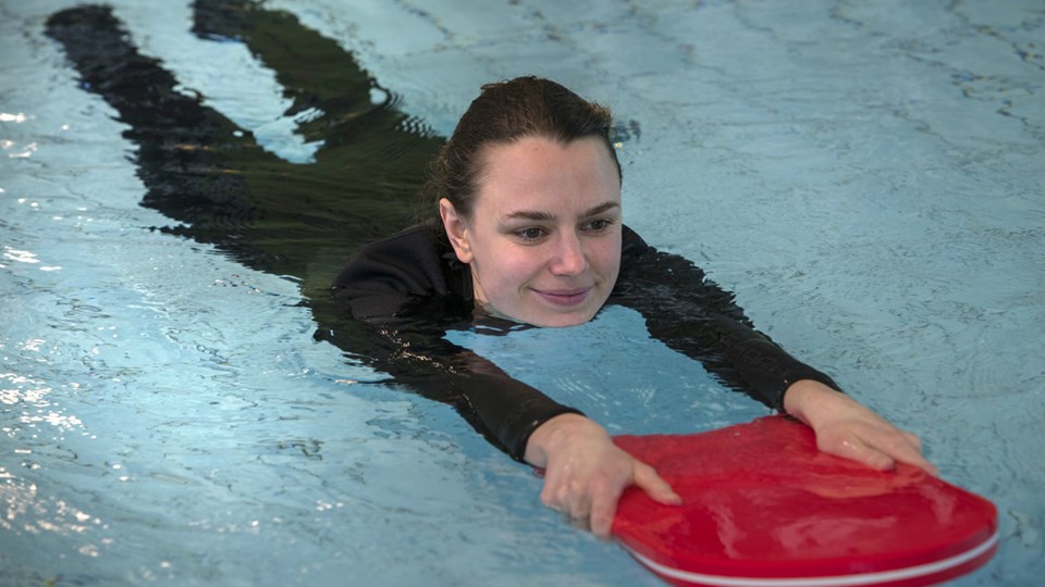En simskolelärare visar hur man simmar med hjälp av ett flythjälpmedel.