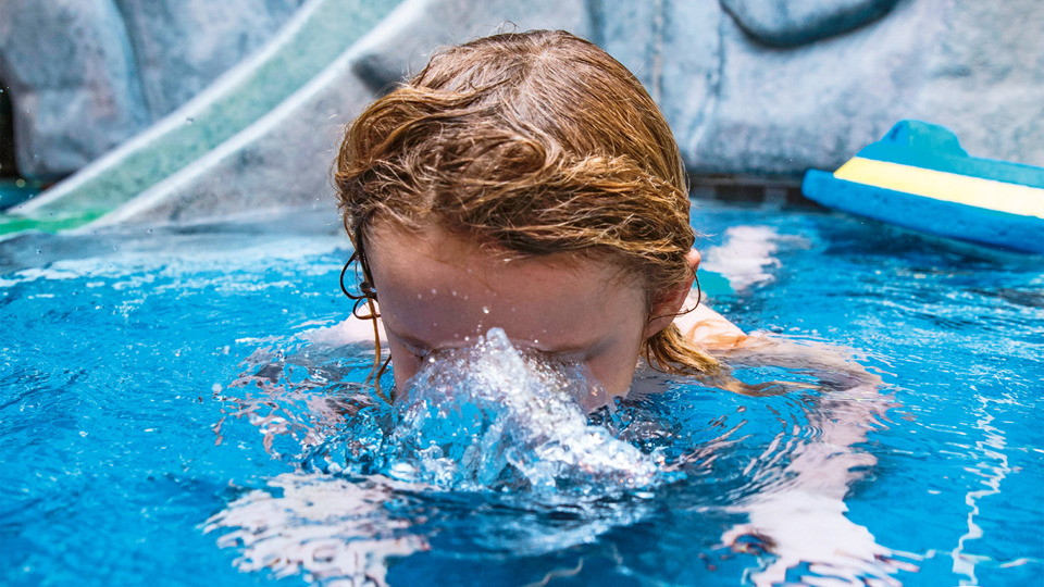 Ett litet barn som övar vattenvana och bubblar med munnen under vattenytan.