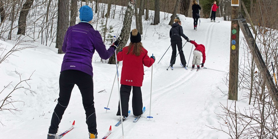 Ett par kvinnor och ett par barn som åker längdskidor i ett skidspår.