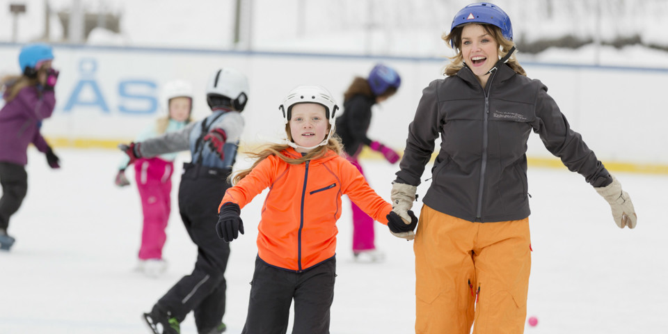 En kvinna och en flicka som åker skridskor hand i hand och ser glada ut.