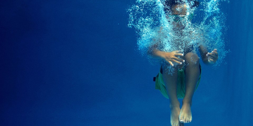 En undervattensbild av ett barn som just landat i vattnet i en bassäng.