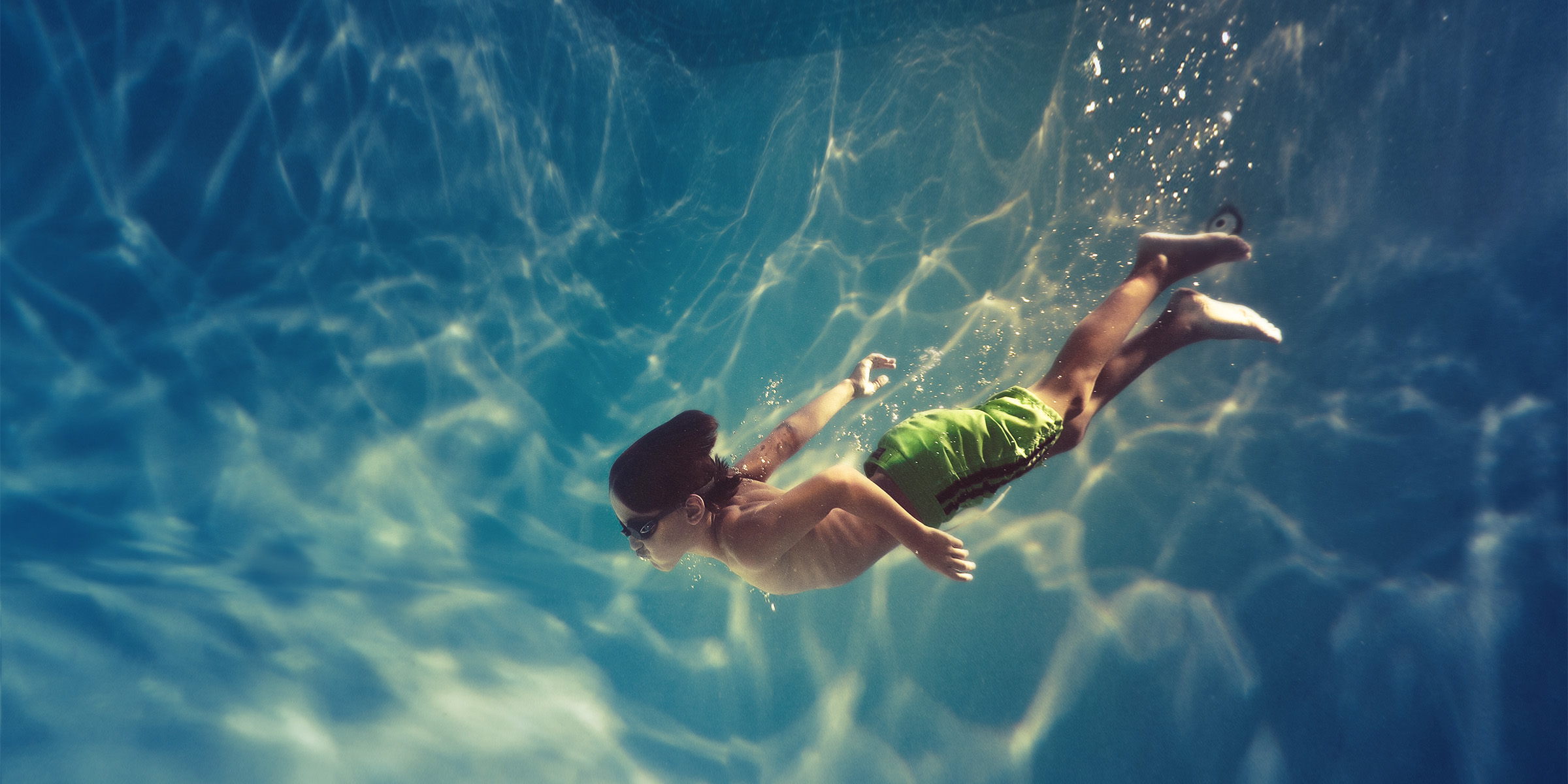 Pojke som simmar under vattnet i en simbassäng.