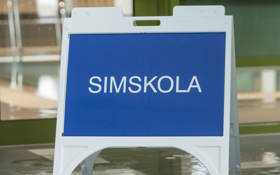 En skylt som det står "Simskola" på, med en bassäng i bakgrunden.