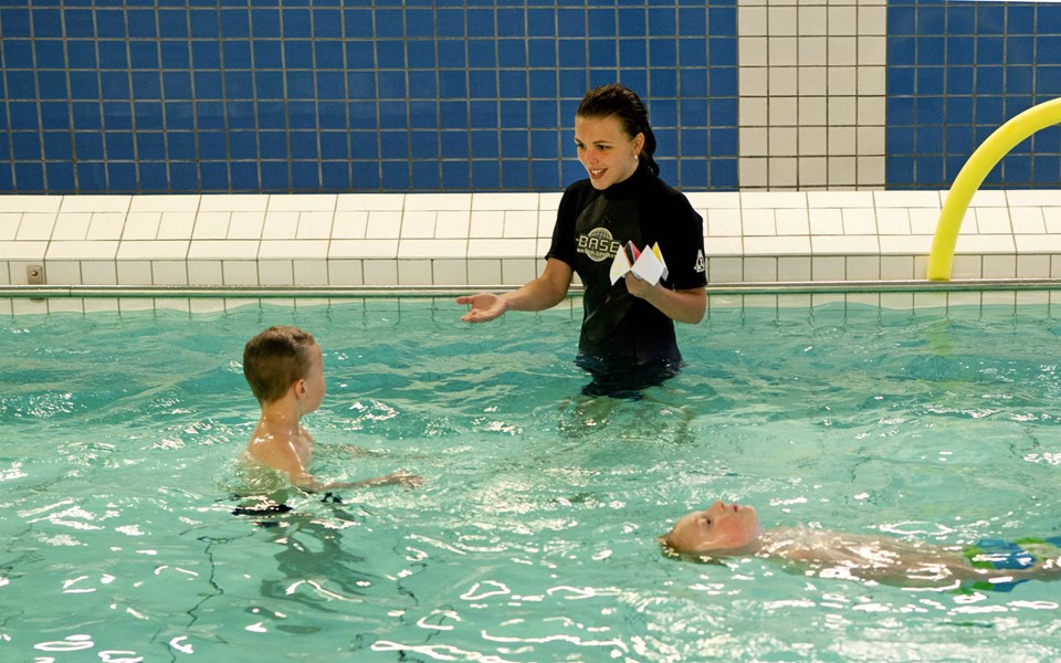 En simlärare som ger instruktioner till ett barn i en simbassäng.