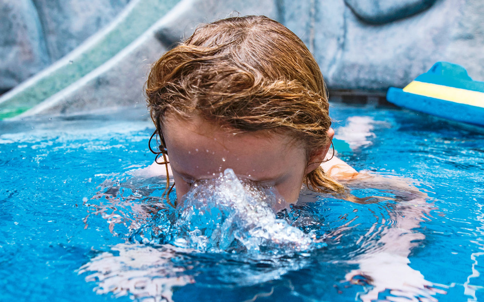 Ett litet barn som övar vattenvana och bubblar med munnen under vattenytan.