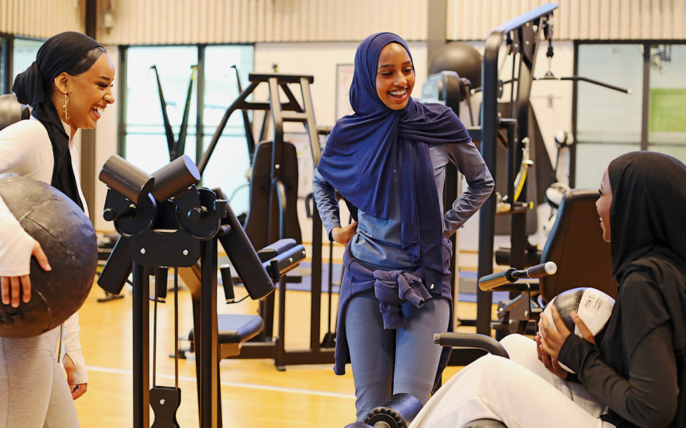 Tre unga tjejer som pratar och skrattar i ett gym.