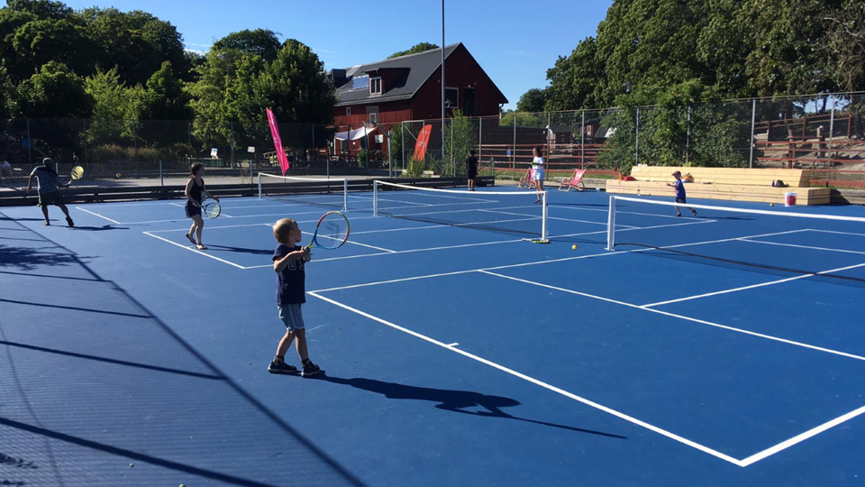 Blå-tennisbanor-barn-spelar-tennis-i-solen