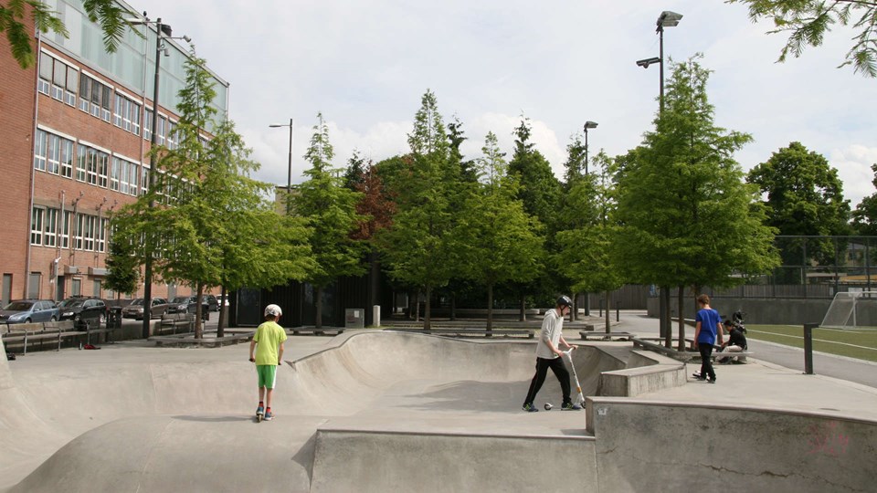 Barn på sparkcyklar i skejtboardpooler i en modern park.