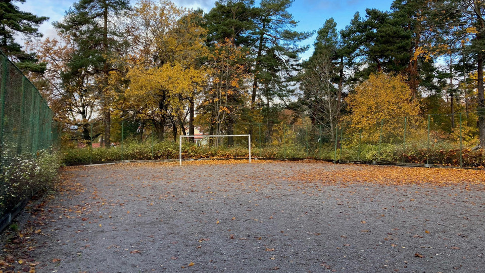 Grusplan omgärdad av högt stänglse. Ett fotbollsmål.