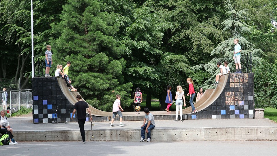 Barn och ungdomar på en skejtboardramp i en lummig park.