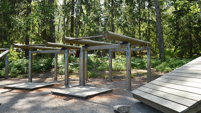 Diverse motionsredskap i trä placerade på en grusplan i skogen